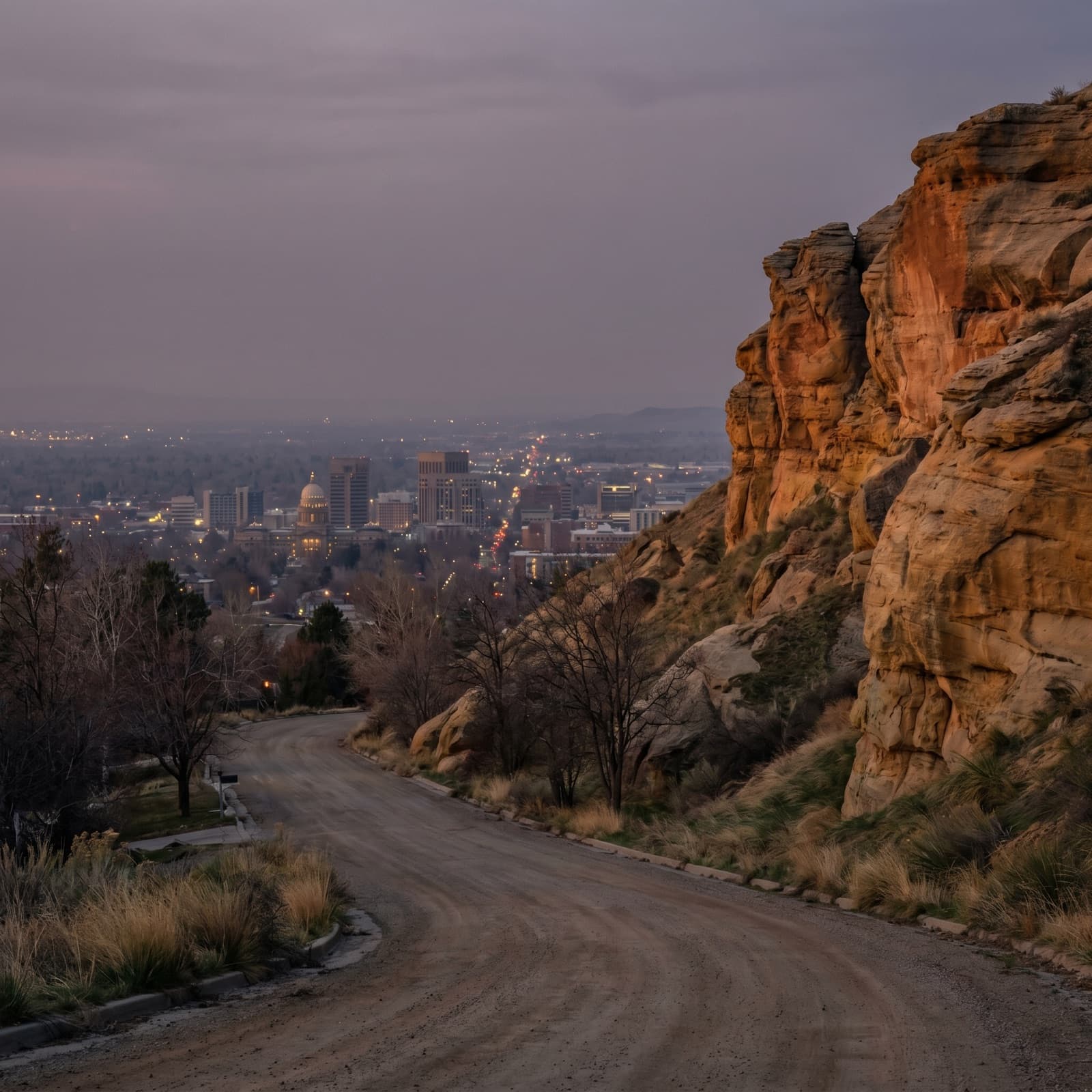 Boise, ID — Table Rock at last light seen from a quiet Boise foothills street, the sandstone mesa and its small white summit cross catching the final warm glow above the valley, the Idaho State Capitol dome just visible downtown in the midground below, dark power lines crossing the foreground, no hikers, no cars, the everyday angle a North End resident actually sees walking home at dusk.